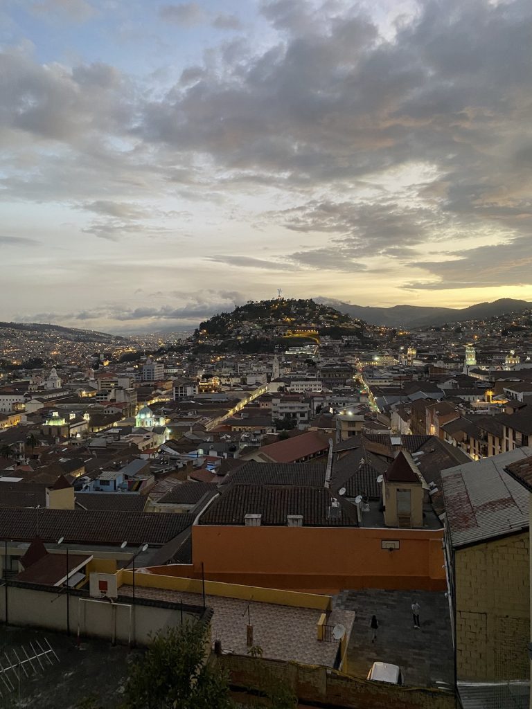 Vista panorâmica de Quito ao entardecer, com telhados históricos, bairros nas encostas e montanhas ao redor, durante extensão de cruzeiro em Galápagos com nossa agência